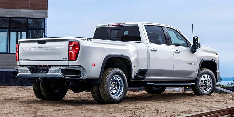 Rear-three-quarter view of a white Chevrolet Silverado LTZ dually pickup truck parked at a dirt construction site.