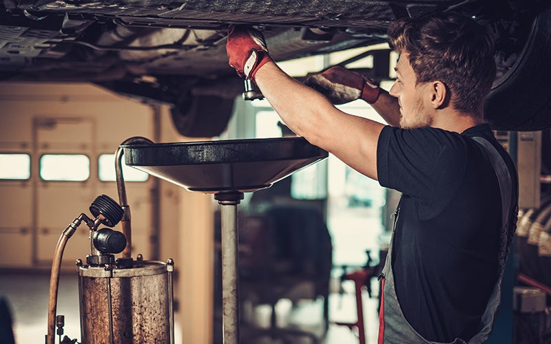A mechanic working underneath a vehicle raised on a lift during an oil change service.